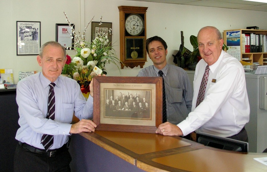 Matthews Real Estate Pic 1 - Trevor Russell and Ken Matthews with a picture of Robert Matthews sitting on the board of the REIQ in the 1930s