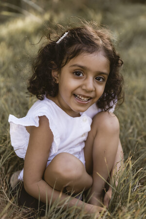 Joanna Kate Photography Pic 5 - Young girl crouched in the grass and smiling at camera during a family photo shoot in Brisbane Queensland